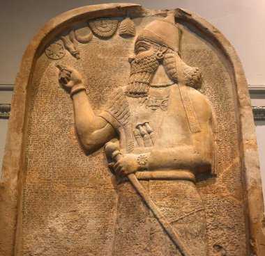 LONDRA BİRLİK KINGDOM 06 17 2023: Ashurnasirpal II kireçtaşı stela: oyulmuş; kral kraliyet şapkasını konik bir üst ile giyer ve otoriteyi sembolize eden bir gürz tutar