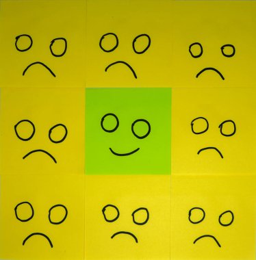 Emotions concept. Background of sticky notes. Green sticky note is among yellow sticky notes.