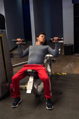 Modern bir spor salonunda dambılla spor yapan eşcinsel bir adam..