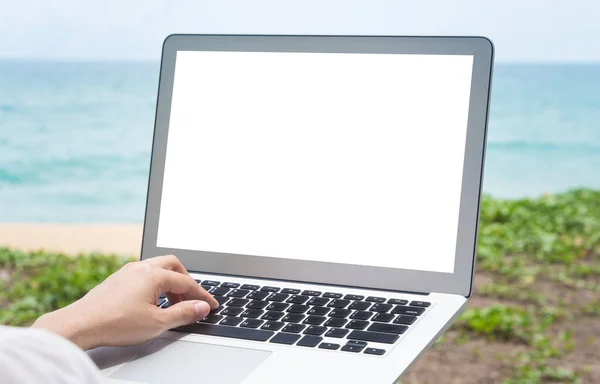 The laptop has a blank screen with morning light against the beach and sea background.Blank screen with clipping path on screen for your advertising.