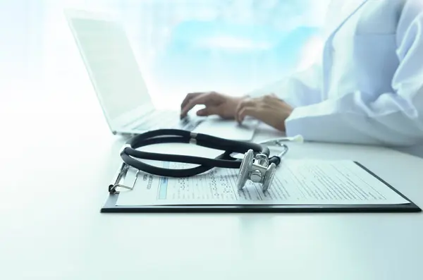医学ドキュメントと病院のバックグラウンドを持つラップトップコンピュータで作業する医師の診察 医学コンセプト ロイヤリティフリーのストック画像