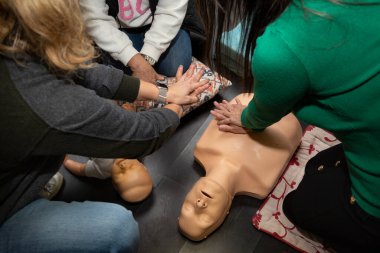 Üç kişi ilk yardım ve suni teneffüs pratiği yapıyor. Bir yetişkin manikini ve bir bebek diriltme manikini ile.