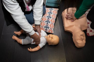 Üç kişi ilk yardım ve suni teneffüs pratiği yapıyor. Bir yetişkin manikini ve bir bebek diriltme manikini ile.