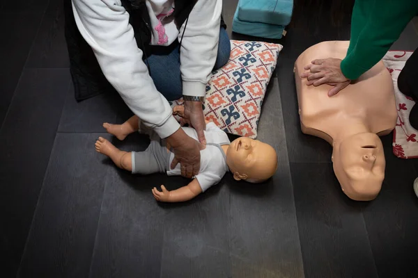 Three people practice first aid and CPR with an adult CPR manikin and another baby resuscitation manikin