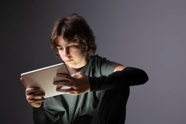 Genç bir kız loş bir odada elinde tabletle ya da elektronik aletle internette geziniyor.