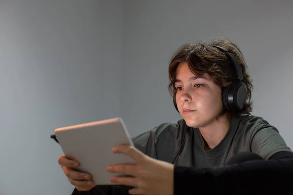 A teenage girl surfs the internet with a tablet or electronic device in a dimly lit room