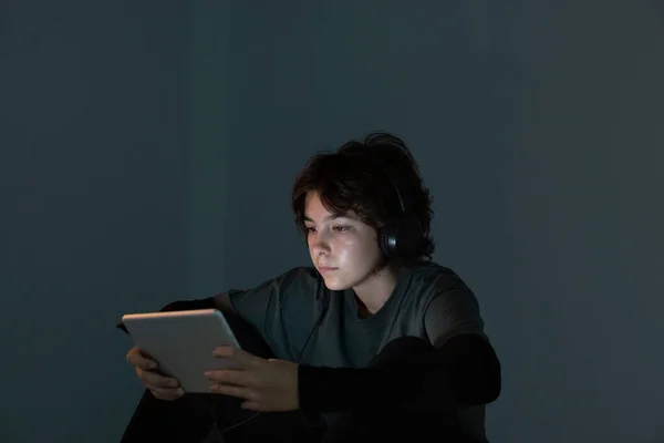 A teenage girl surfs the internet with a tablet or electronic device in a dimly lit room