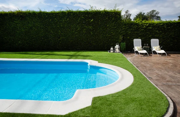 Terrace with pool, lawn, hedge and two white loungers