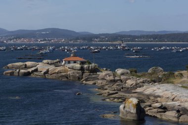 View of the Punta Cabalo lighthouse on the Illa de Arousa with fishing boats in the background clipart