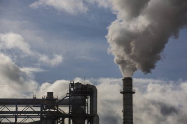 Ahşap işleme fabrikasının bacası. Beyaz bulutlu mavi gökyüzünde beyaz dumanlı baca