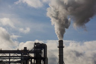 Ahşap işleme fabrikasının bacası. Beyaz bulutlu mavi gökyüzünde beyaz dumanlı baca