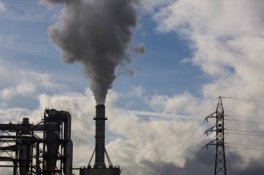 Ahşap işleme endüstrisinden çıkan dumanlı baca ve elektrik direği. Mavi gökyüzü ve beyaz bulutlu elektrik. Kirlilik