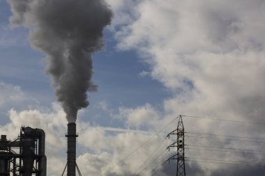 Ahşap işleme endüstrisinden çıkan dumanlı baca ve elektrik direği. Mavi gökyüzü ve beyaz bulutlu elektrik. Kirlilik