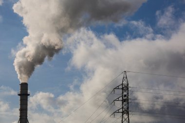 Ahşap işleme endüstrisinden çıkan dumanlı baca ve elektrik direği. Mavi gökyüzü ve beyaz bulutlu elektrik. Kirlilik