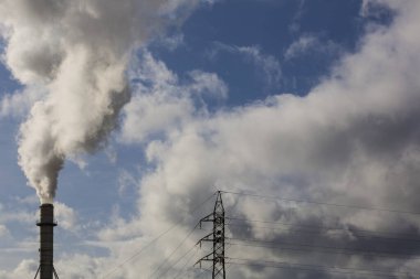 Ahşap işleme endüstrisinden çıkan dumanlı baca ve elektrik direği. Mavi gökyüzü ve beyaz bulutlu elektrik. Kirlilik