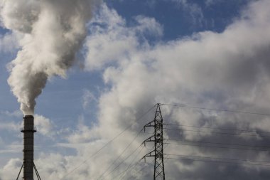 Ahşap işleme endüstrisinden çıkan dumanlı baca ve elektrik direği. Mavi gökyüzü ve beyaz bulutlu elektrik. Kirlilik