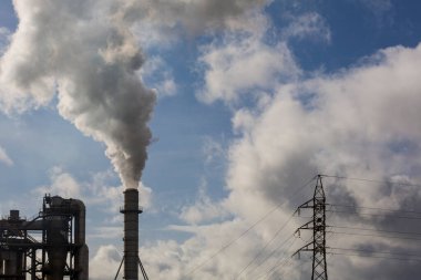 Ahşap işleme endüstrisinden çıkan dumanlı baca ve elektrik direği. Mavi gökyüzü ve beyaz bulutlu elektrik. Kirlilik