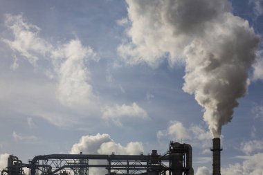 Ahşap işleme fabrikasının bacası. Beyaz bulutlu mavi gökyüzünde beyaz dumanlı baca