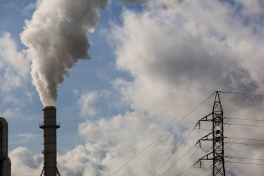 Ahşap işleme endüstrisinden çıkan dumanlı baca ve elektrik direği. Mavi gökyüzü ve beyaz bulutlu elektrik. Kirlilik