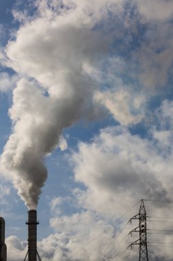 Ahşap işleme endüstrisinden çıkan dumanlı baca ve elektrik direği. Mavi gökyüzü ve beyaz bulutlu elektrik. Kirlilik
