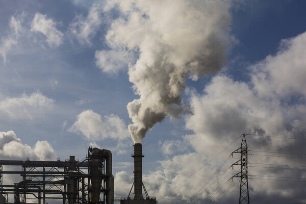 Chimney with smoke from a wood processing industry and an electric power pole. Electricity with blue sky and white clouds. Pollution