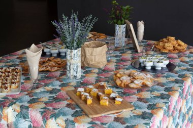 Çeşitli geleneksel Galiçya tatlıları olan bir masa. Karnaval tatlıları. Santiago pastası, karnaval kulakları, karnaval çiçekleri, çay kekleri, meyve bardakları ve aperatifler. Ortanca çiçekli renkli bir masa örtüsü..