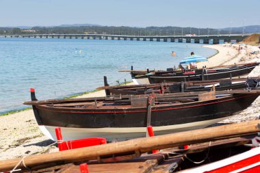 Arousa Adası 'ndaki O Bao plajında tahta dornalar. Geleneksel tekneler. Arousa Adası 'na geçiş köprüsü.