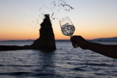 Birisi arka planda San Sadurninho kulesi olan bir bardak Albarinho şarabı dolduruyor. Gün batımında siluet.