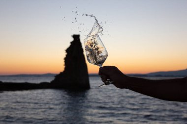 Birisi arka planda San Sadurninho kulesi olan bir bardak Albarinho şarabı dolduruyor. Gün batımında siluet.