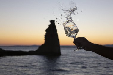 Birisi arka planda San Sadurninho kulesi olan bir bardak Albarinho şarabı dolduruyor. Gün batımında siluet.