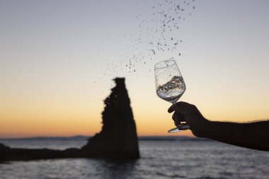Birisi arka planda San Sadurninho kulesi olan bir bardak Albarinho şarabı dolduruyor. Gün batımında siluet.