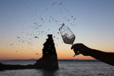 Birisi arka planda San Sadurninho kulesi olan bir bardak Albarinho şarabı dolduruyor. Gün batımında siluet.