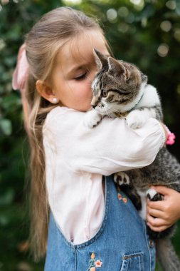 Doğada küçük bir kızın kollarında tatlı bir kedi oturuyor.