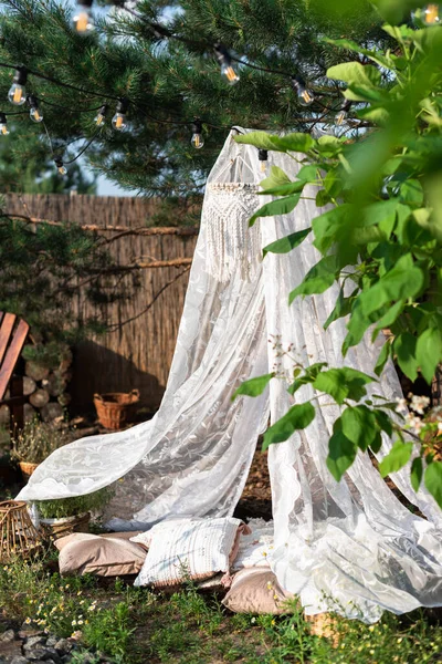 庭の松の木からシャンデリアとクッション付きの白いネットキャノピーがかかっています — ストック写真