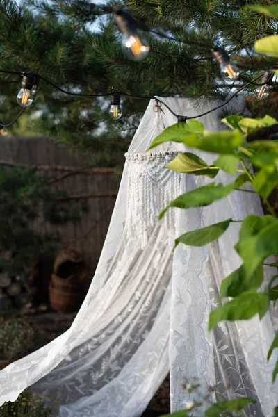 花园里一棵松树上挂着一个白色的网罩 上面挂着吊灯和垫子 — 图库照片