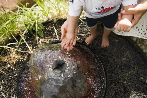 Bir annenin elleri dekoratif, küçük, dairesel bir bahçede bir çocuğun küçük ellerini tutar.