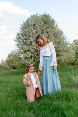 A mother with a little daughter on a walk among a green meadow and a blooming pear tree clipart