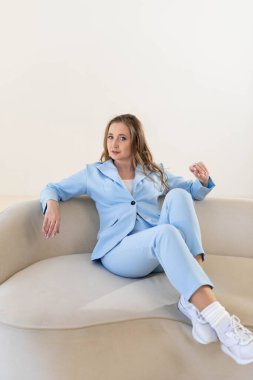 Sarı saçlı, mavi takım elbiseli güzel bir kadın açık bir kanepede oturuyor.