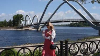 Genç bir kız nehir kenarındaki bir köprünün arkasındaki plastik bir şişeden su içiyor.