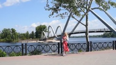 Güneş gözlüklü genç bir kadın şehirde yürürken plastik bir şişeden su içiyor.