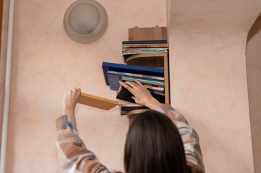 Uzun saçlı serbest çalışan bir kadın kitaplıktan kitap alıyor.