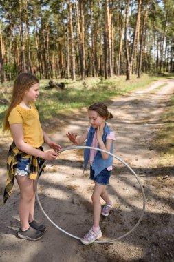 Okul çağındaki tatlı kızlar ormanda bir patikada jimnastik metal bir çemberle oynuyorlar.