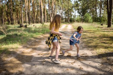 Okul çağındaki tatlı kızlar ormanda bir patikada jimnastik metal bir çemberle oynuyorlar.