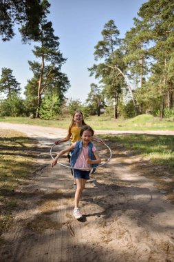 Okul çağındaki tatlı kızlar ormanda bir patikada jimnastik metal bir çemberle oynuyorlar.