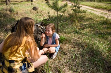 Ormanda büyüteçle ağaçların yanında oturan iki neşeli kız öğrenci.