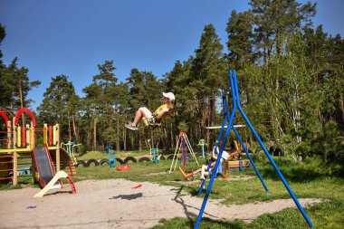 İki sarışın liseli kız salıncakta sallanıyor bir çocuk parkında çam ormanının yakınında