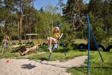 İki sarışın liseli kız salıncakta sallanıyor bir çocuk parkında çam ormanının yakınında