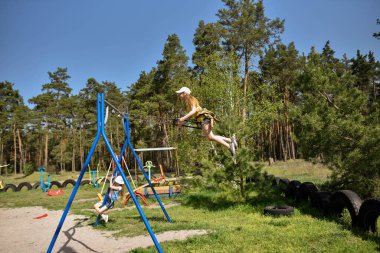 İki sarışın liseli kız salıncakta sallanıyor bir çocuk parkında çam ormanının yakınında