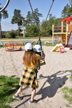 İki sarışın liseli kız salıncakta sallanıyor bir çocuk parkında çam ormanının yakınında