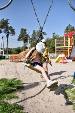 İki sarışın liseli kız salıncakta sallanıyor bir çocuk parkında çam ormanının yakınında